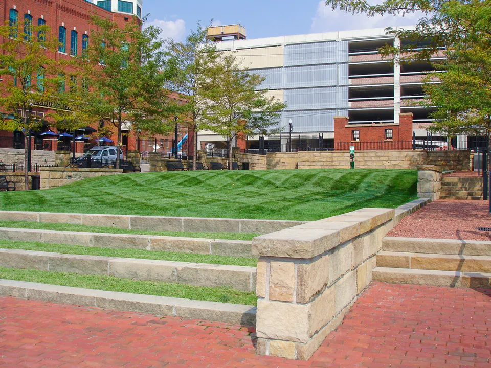 Commercial courtyard with stepped lawn, stone retaining walls, brick walks, railings, and street trees.